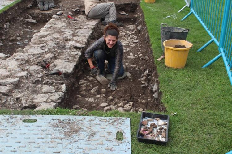 Helen cleans the cobbled surface on the exterior of the building in Trench 2
